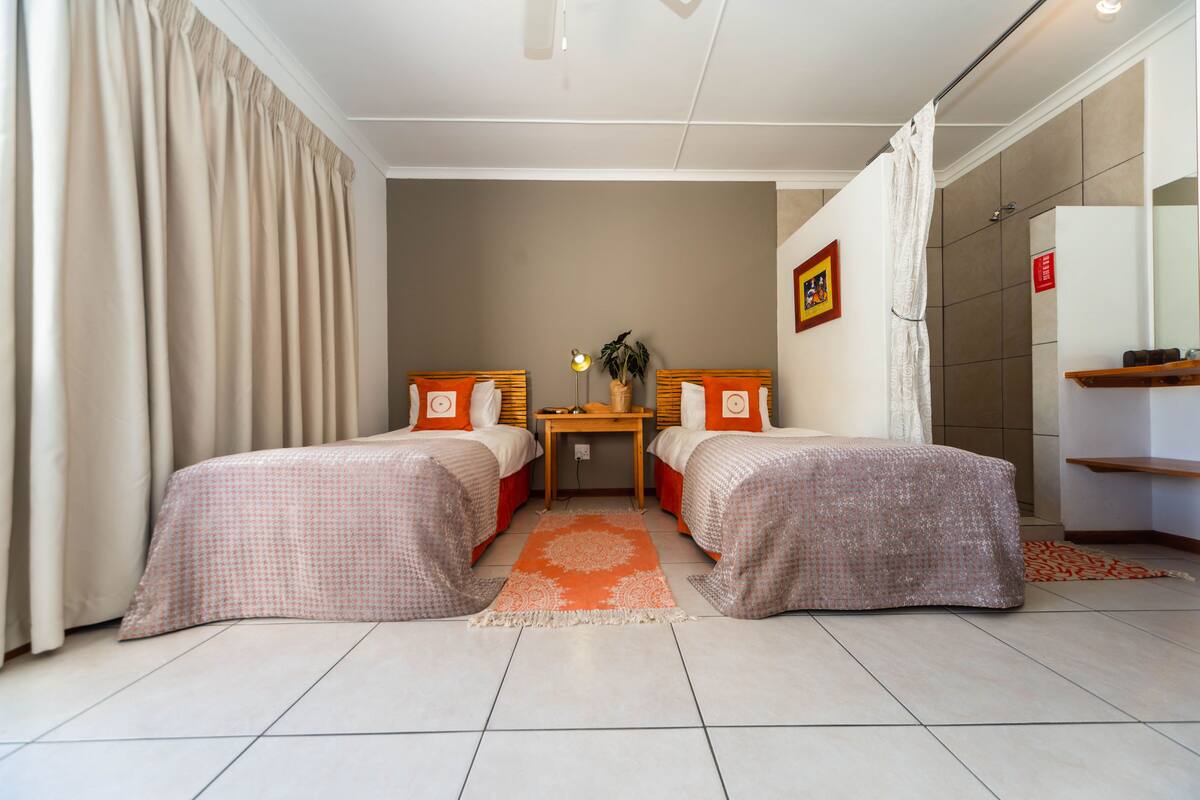 A hotel room with two beds, a small table with a lamp, and a mirror on the wall.