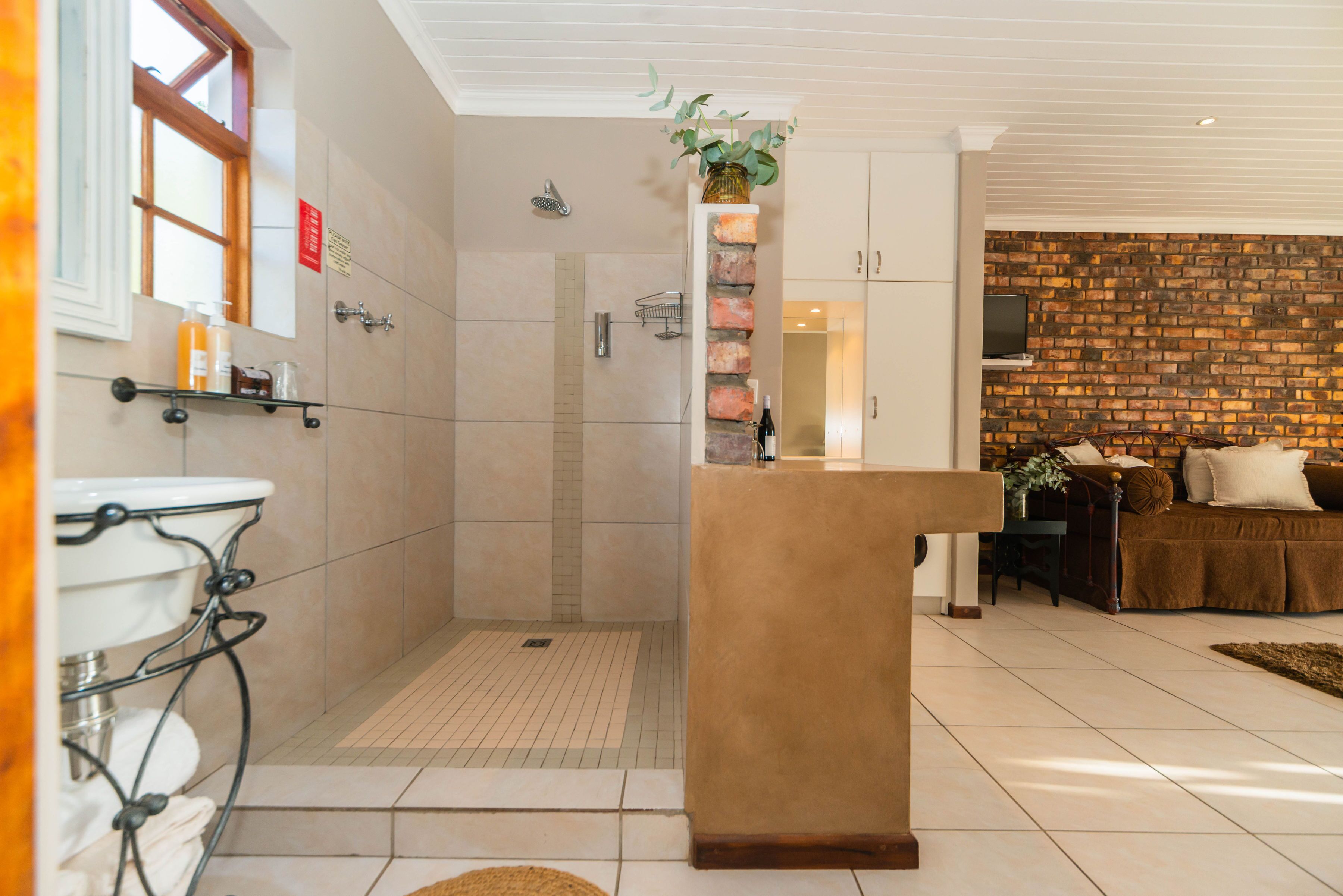 Un baño moderno con ducha, lavabo y tocador. Hay una pared decorativa de ladrillo y una zona de estar con sofá y mesa de centro en la sala.