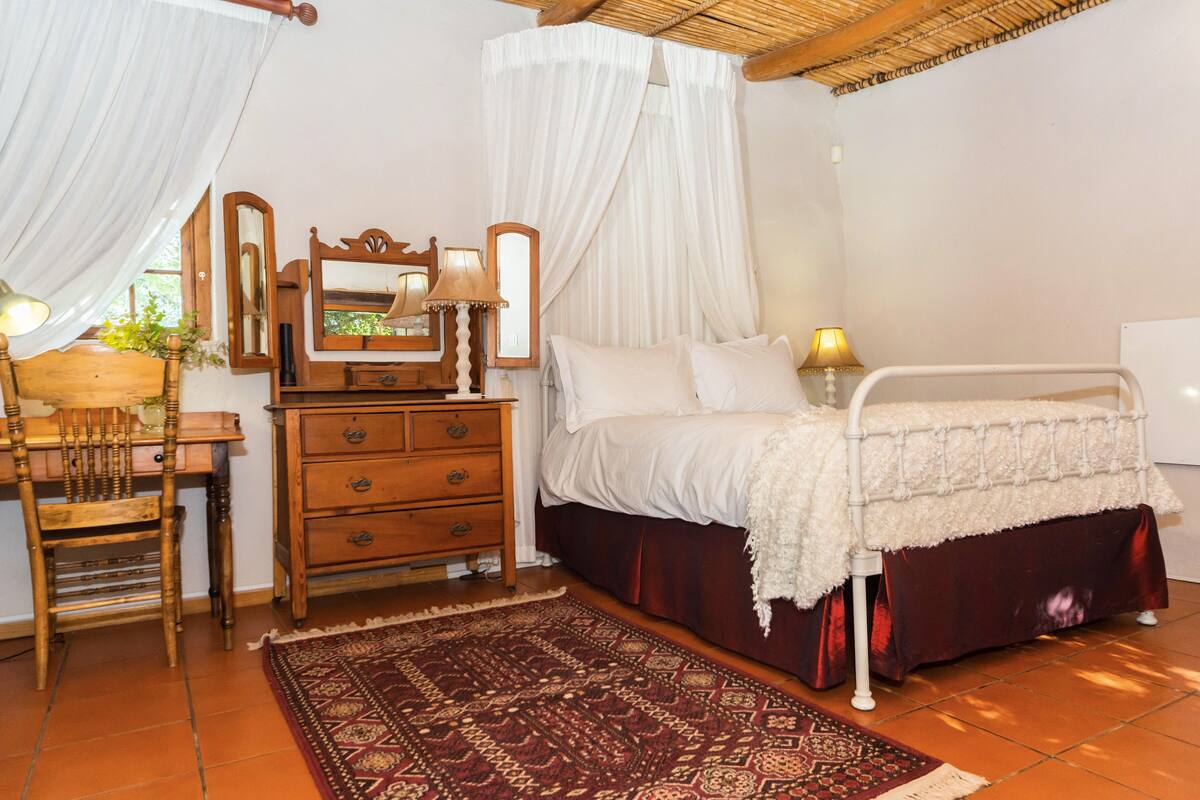 A bedroom with a bed, a wooden dresser, a mirror, a chair, and a patterned rug.