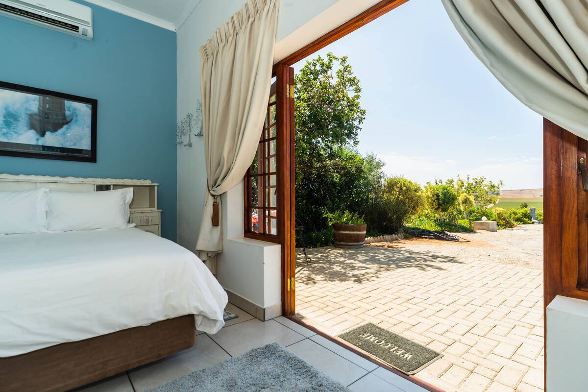 A bedroom with a bed, a window with curtains, and a view of a garden and landscape.