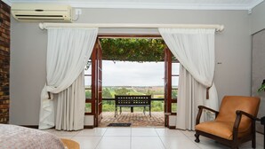 Una habitación con un ventanal grande, una banca, una silla y una cama.