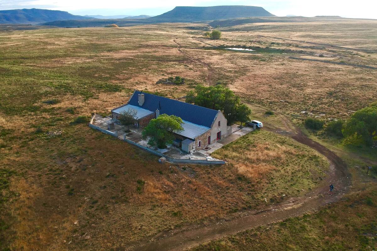 An isolated house with a blue roof, surrounded by a rural landscape with a dirt road and distant hills.