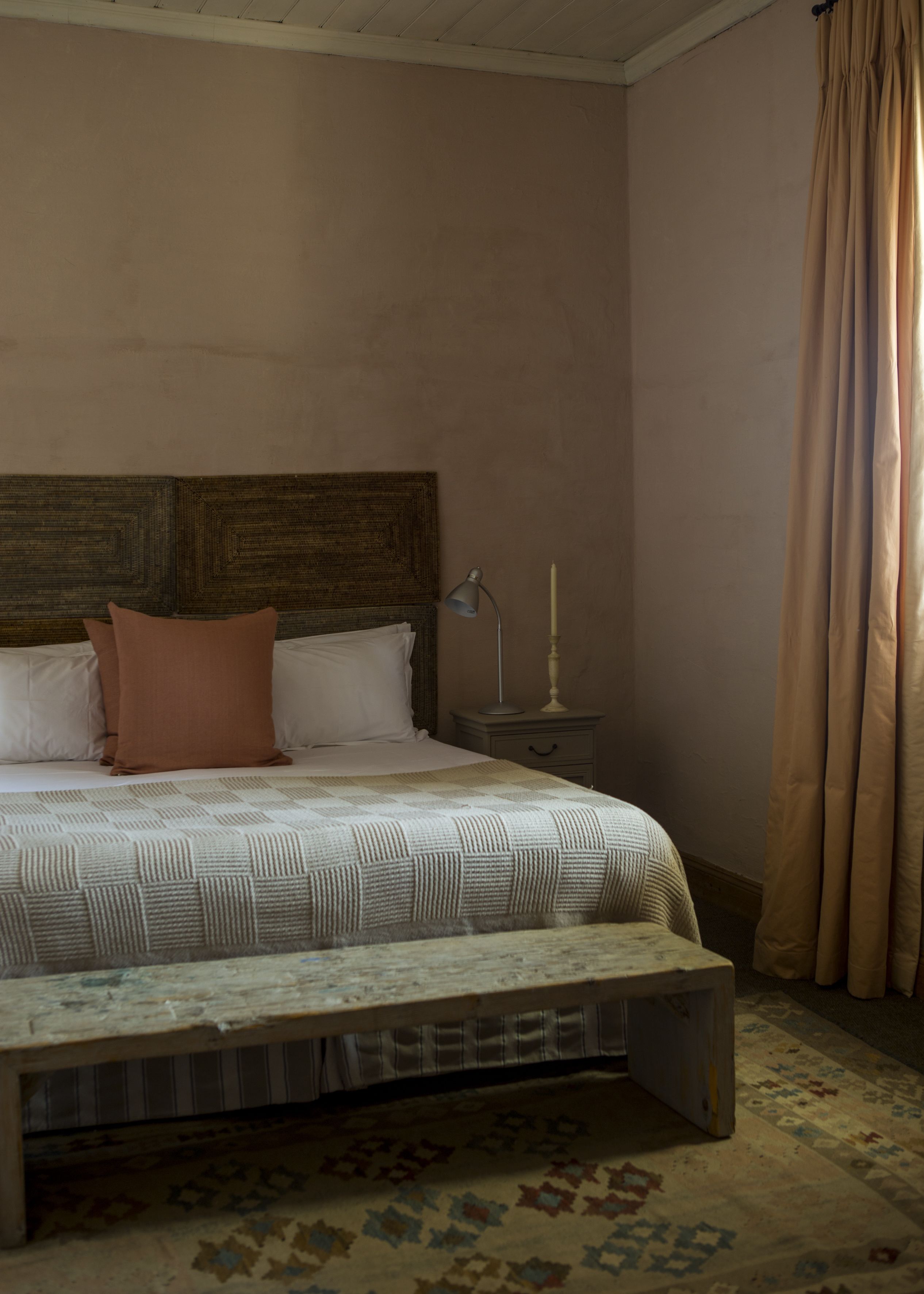 Une chambre à coucher avec une tête de lit en bois, un lit recouvert d’une couvre-lit à motifs, une lampe de chevet et une table de chevet avec une bougie.