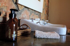 A bathroom with a white sink, two faucets, a bottle of liquid soap, a wicker basket, and a white towel on a dark countertop. - Sneeuberg Nature Reserve (Nieu-Bethesda)