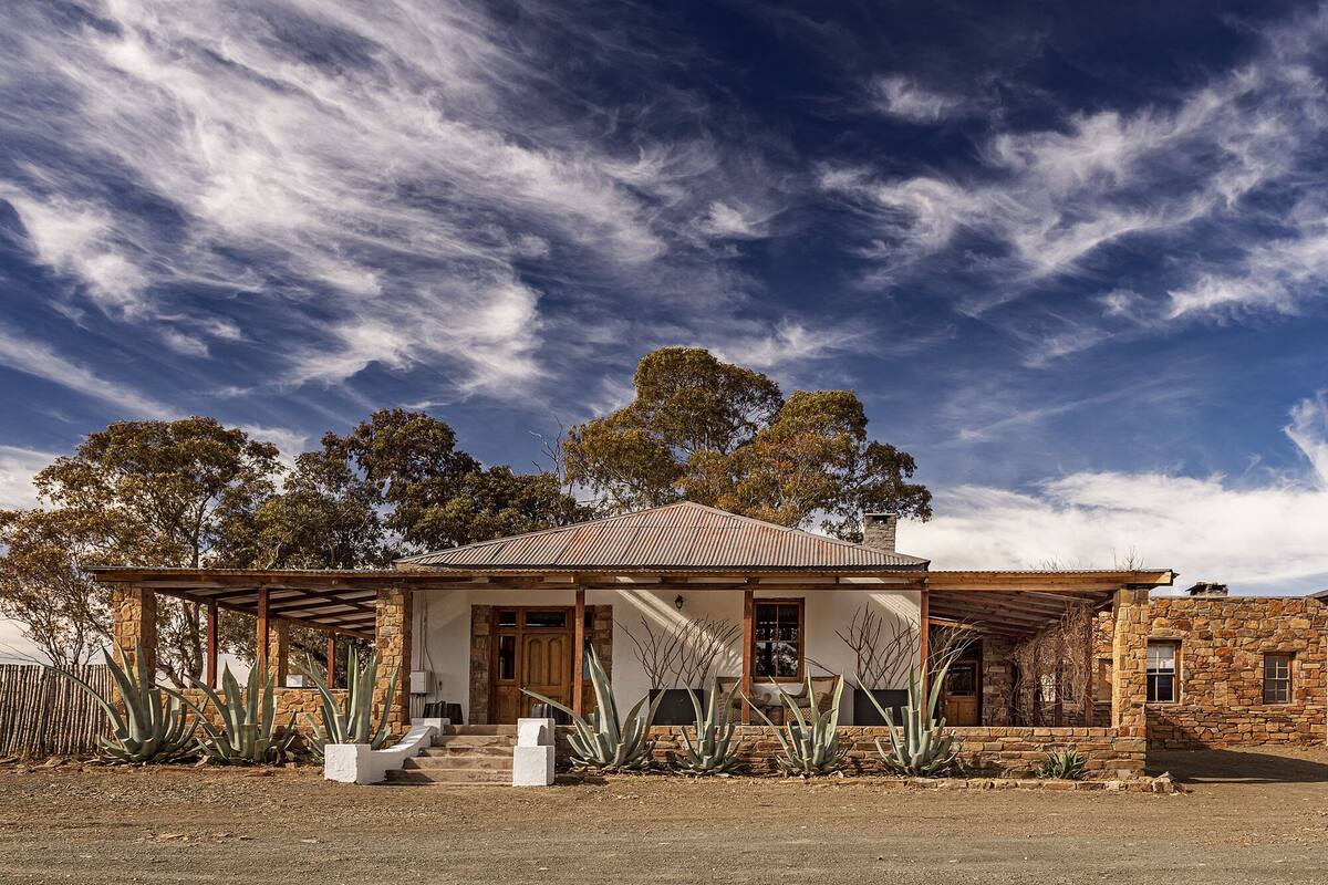 A rustic house with a stone facade, a wooden porch, and a metal roof.