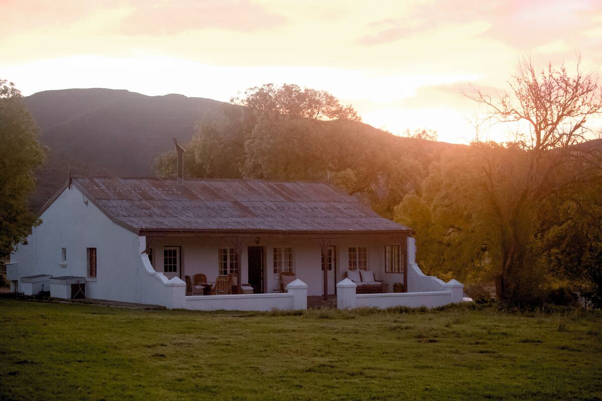 A white house with a sloped roof, a porch with seating, and a small garden area.