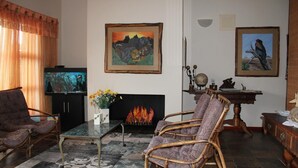 A living room with a fireplace, a television, and two framed paintings. - Marina Martinique B and B (Jeffreys Bay)