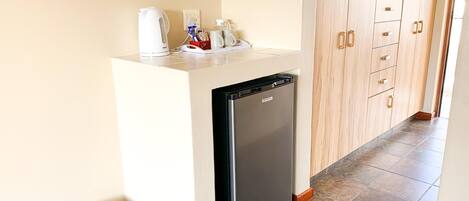 A compact kitchenette with a refrigerator, a kettle, and a coffee maker.