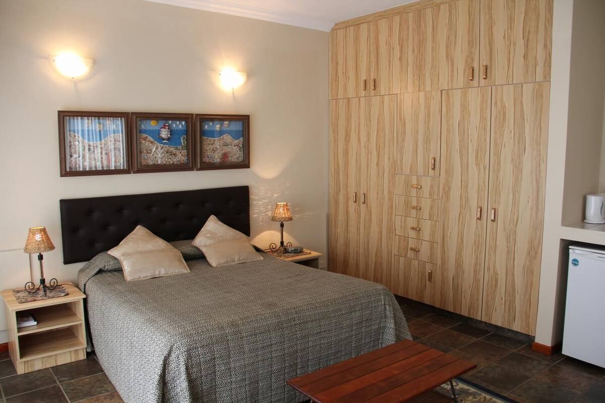 A bedroom with a bed, bedside tables, lamps, a wooden wardrobe, and a small table.