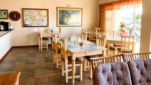 A dining area with a glass-top table, wooden chairs, a ceiling fan, and a large painting on the wall. - Marina Martinique B and B (Jeffreys Bay)