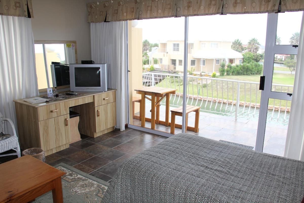 A room with a TV on a wooden cabinet, a small table, and a view of a residential area with a pool.