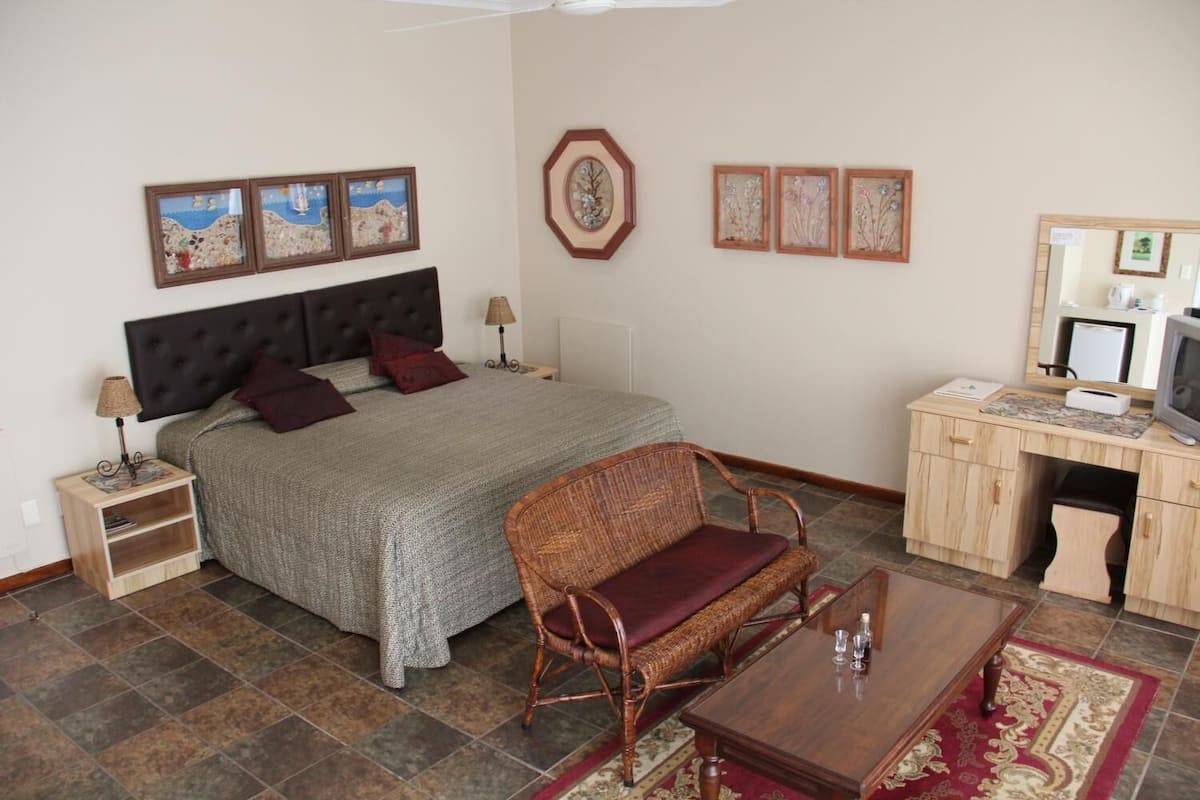 A bedroom with a bed, bedside tables, a chair, a desk with a computer, and artwork on the walls.