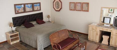 A bedroom with a bed, bedside tables, a chair, a desk with a computer, and artwork on the walls.