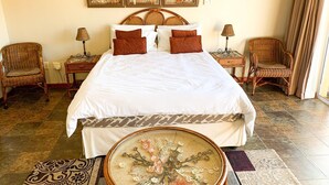 A neatly arranged bedroom with a large bed, two wicker chairs, a small round table, and three framed artworks on the wall. - Marina Martinique B and B (Jeffreys Bay)