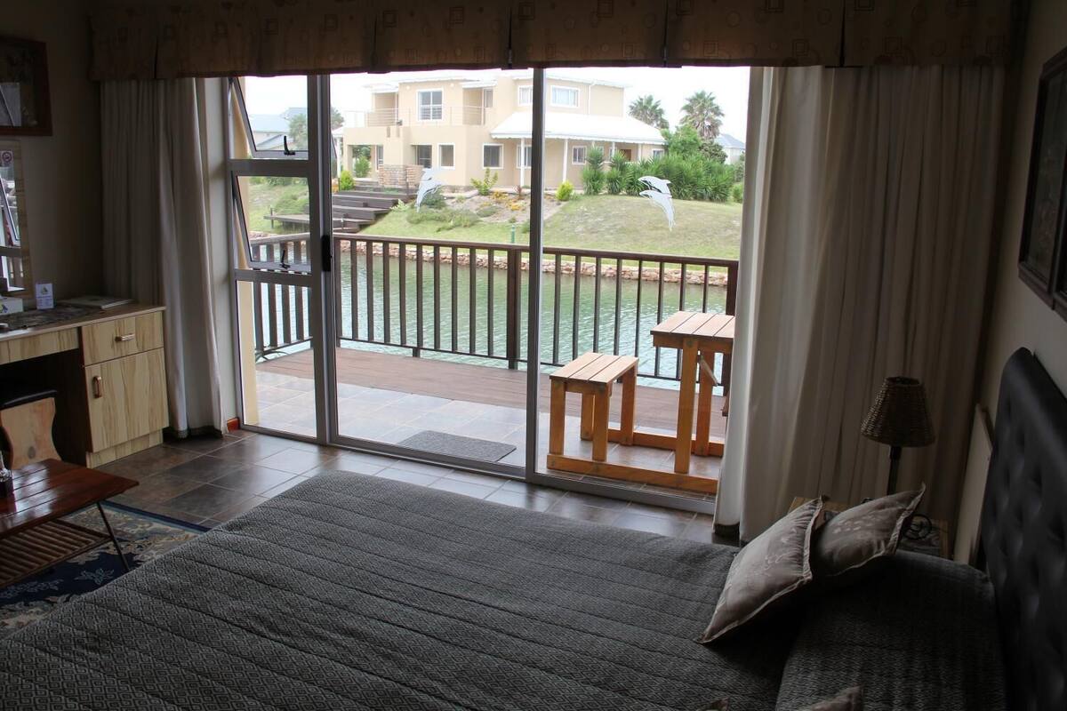 A bedroom with a large sliding glass door leading to a balcony with a view of a residential area and a pool.