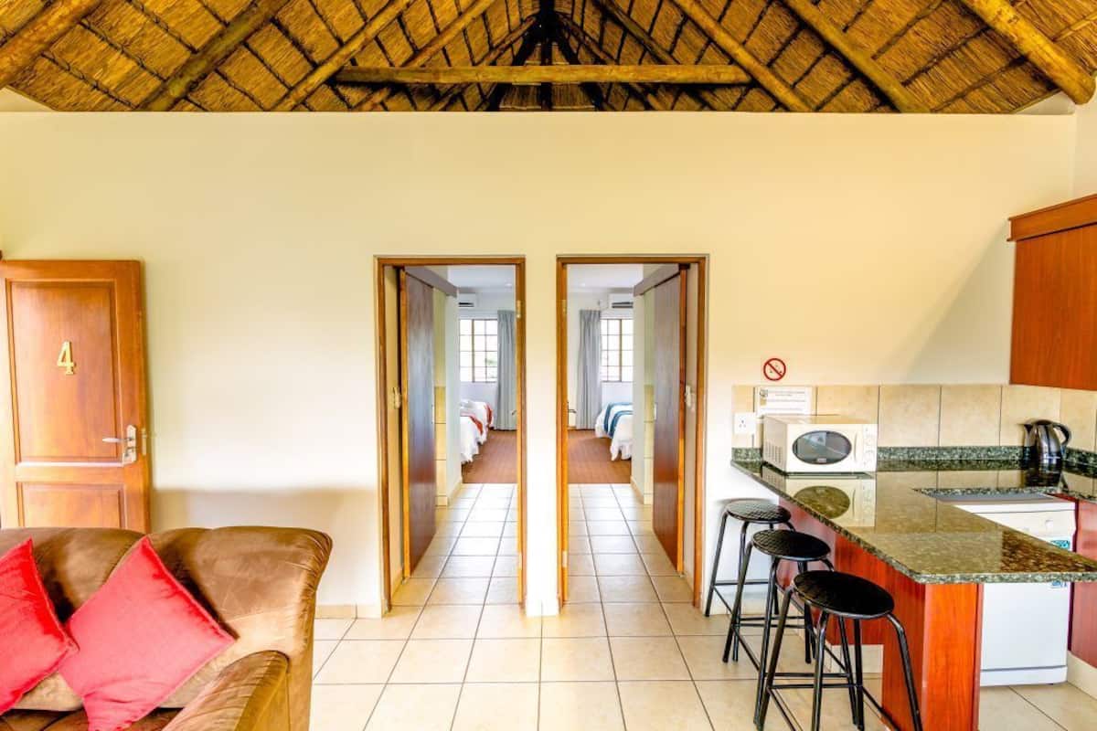 A hotel room with a wooden door marked '4', a sofa with red cushions, a kitchen area with a microwave and a kettle, and a thatched roof ceiling.