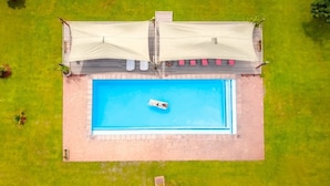 Vue aérienne d’une piscine rectangulaire avec un petit bateau, entourée d’une terrasse aménagée avec des sièges et un espace abrité.