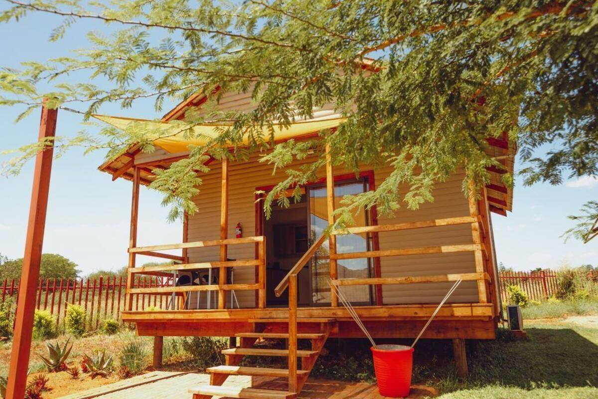 A wooden cabin with a porch, steps, and a red bucket.