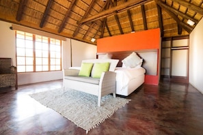 A spacious room with a high ceiling, a large bed with white bedding and green pillows, a wicker sofa, and a large window providing natural light. - Kruger View Chalets (Nkomazi)