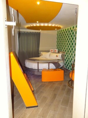 A bedroom with a bed, a small table, a chair, a sofa, a curtain, and a patterned wall.