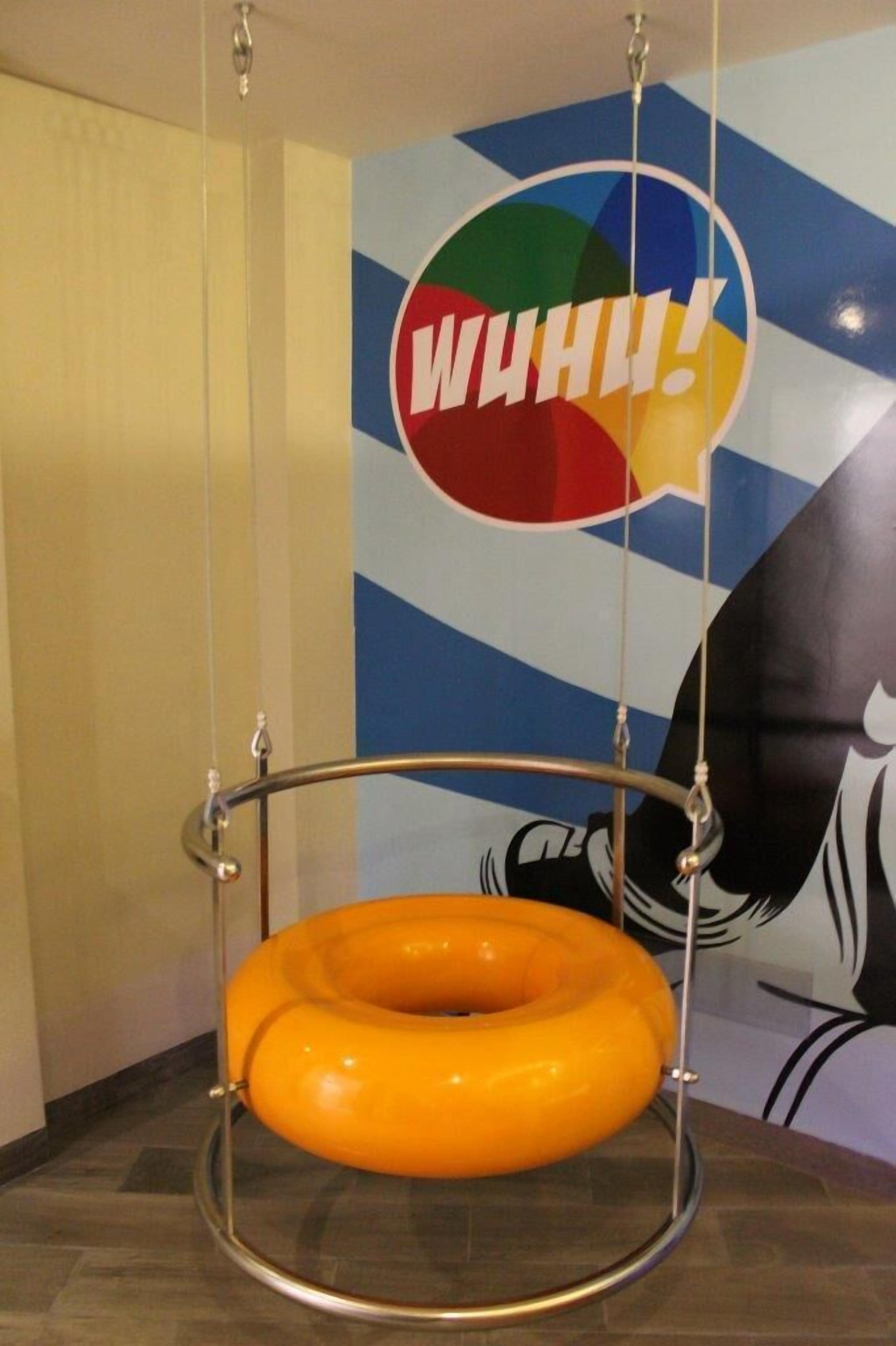 Un sillón naranja colgante en una habitación con un mural de pared colorido y un gran gráfico de bocadillo de diálogo.