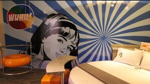 A room with a bed, a wall mural, a hanging chair, and a colorful sign.