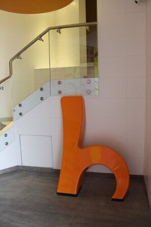 A modern staircase with glass railings and a unique orange letter 'L' sculpture on the floor.