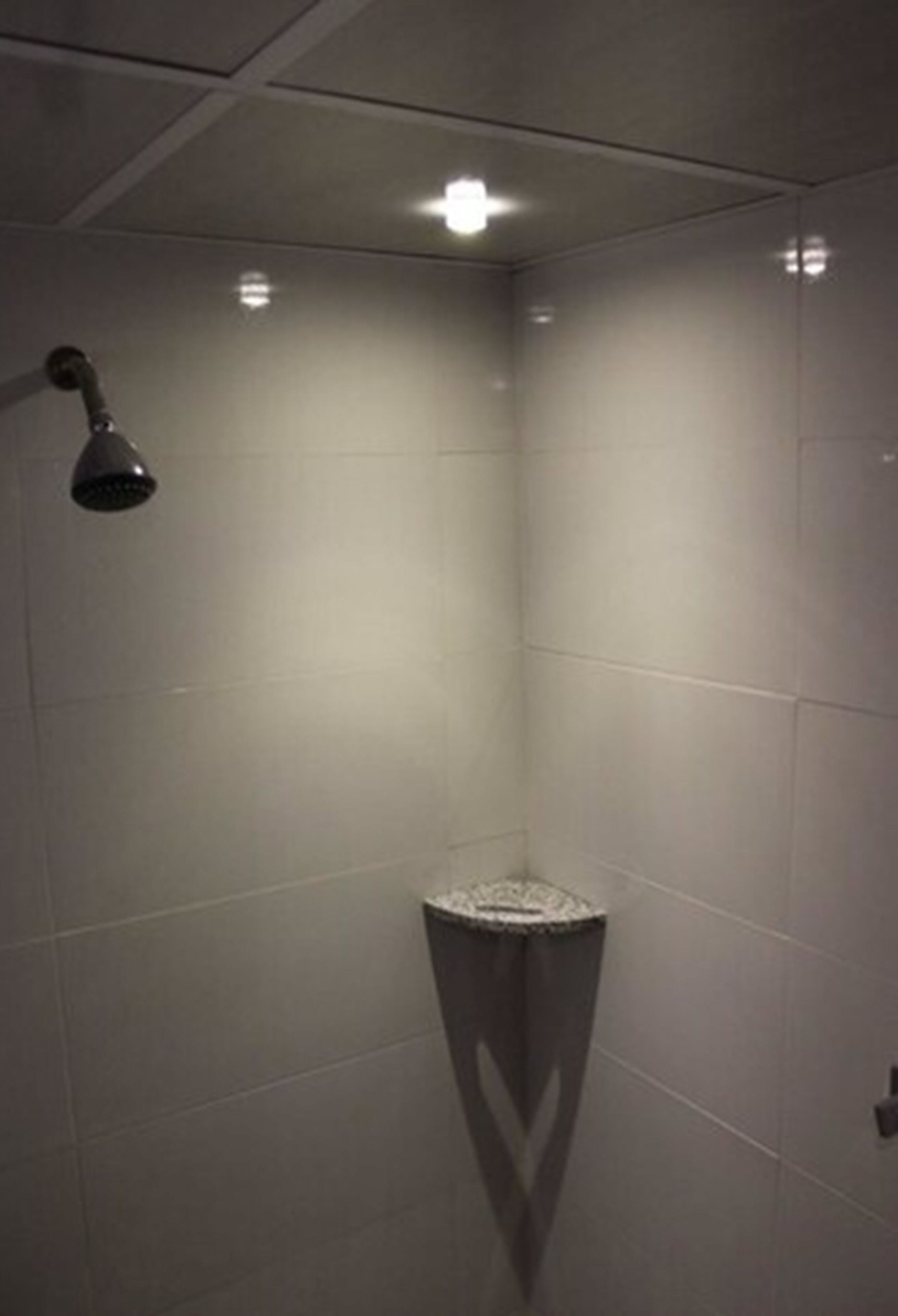 Un espacio de ducha pequeño y cerrado, con una sola luz en el techo y un desagüe en la esquina.