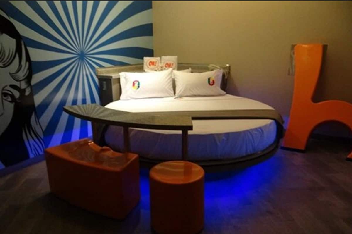 A bed with a round headboard, a nightstand, a chair, and a wall with a blue radial pattern.