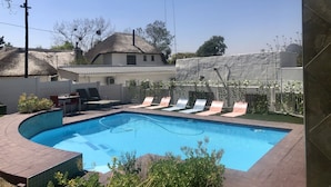 A swimming pool with lounge chairs, a thatched-roof house, and a white building in the background. - Muco Guest House (Sandton)