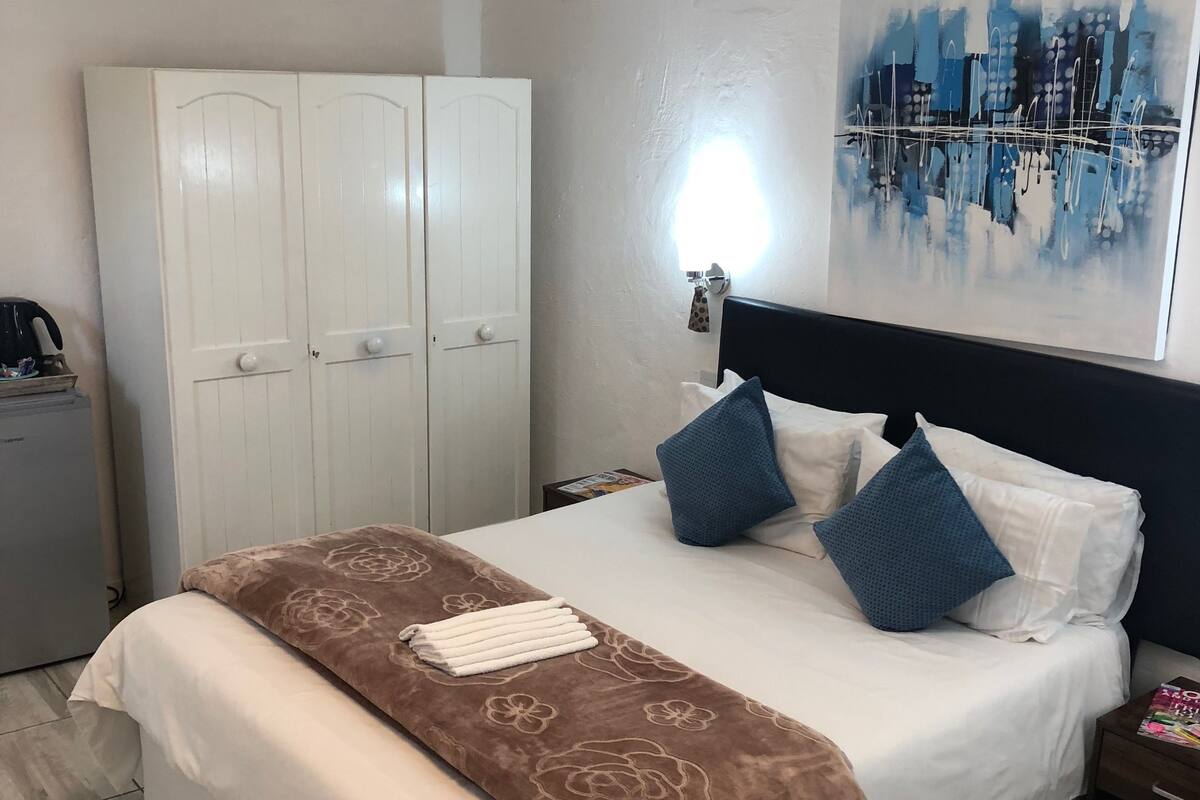 Une chambre à coucher bien rangée, avec un lit, une armoire, une table de chevet et un tableau représentant un paysage urbain accroché au mur.