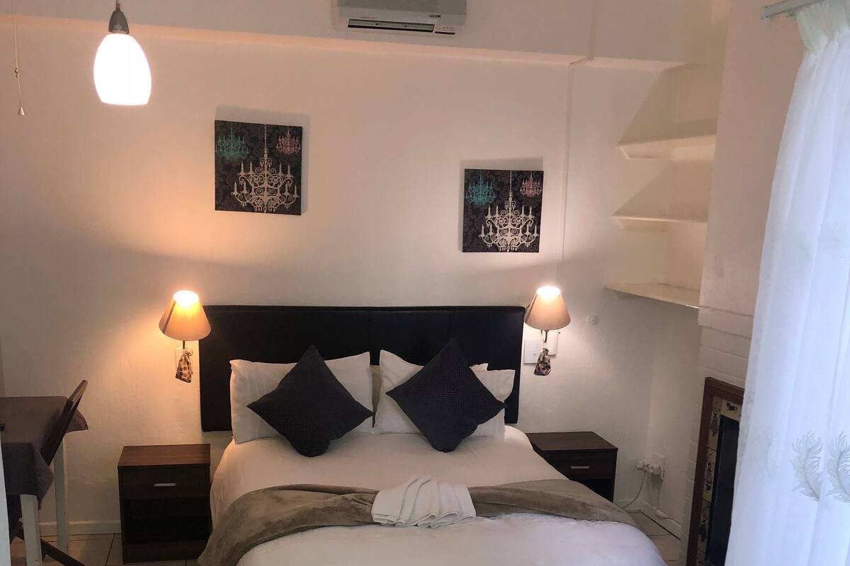 Une chambre à coucher bien aménagée, avec un lit, des lampes de chevet, une tête de lit noire et deux unités de climatisation fixées au mur.