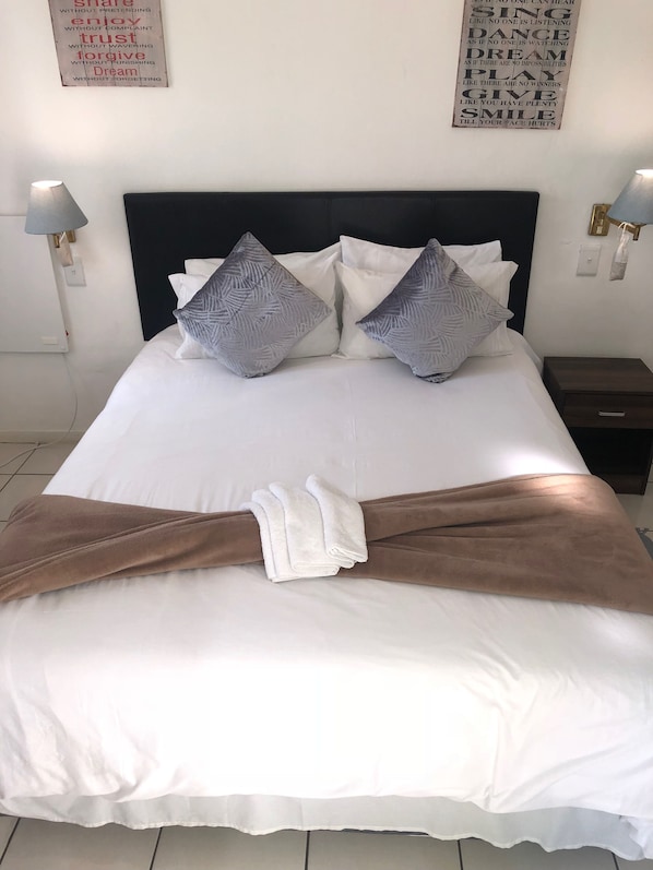 A neatly made bed with white and brown linens, two patterned pillows, and a towel draped over the foot of the bed. - Muco Guest House (Sandton)