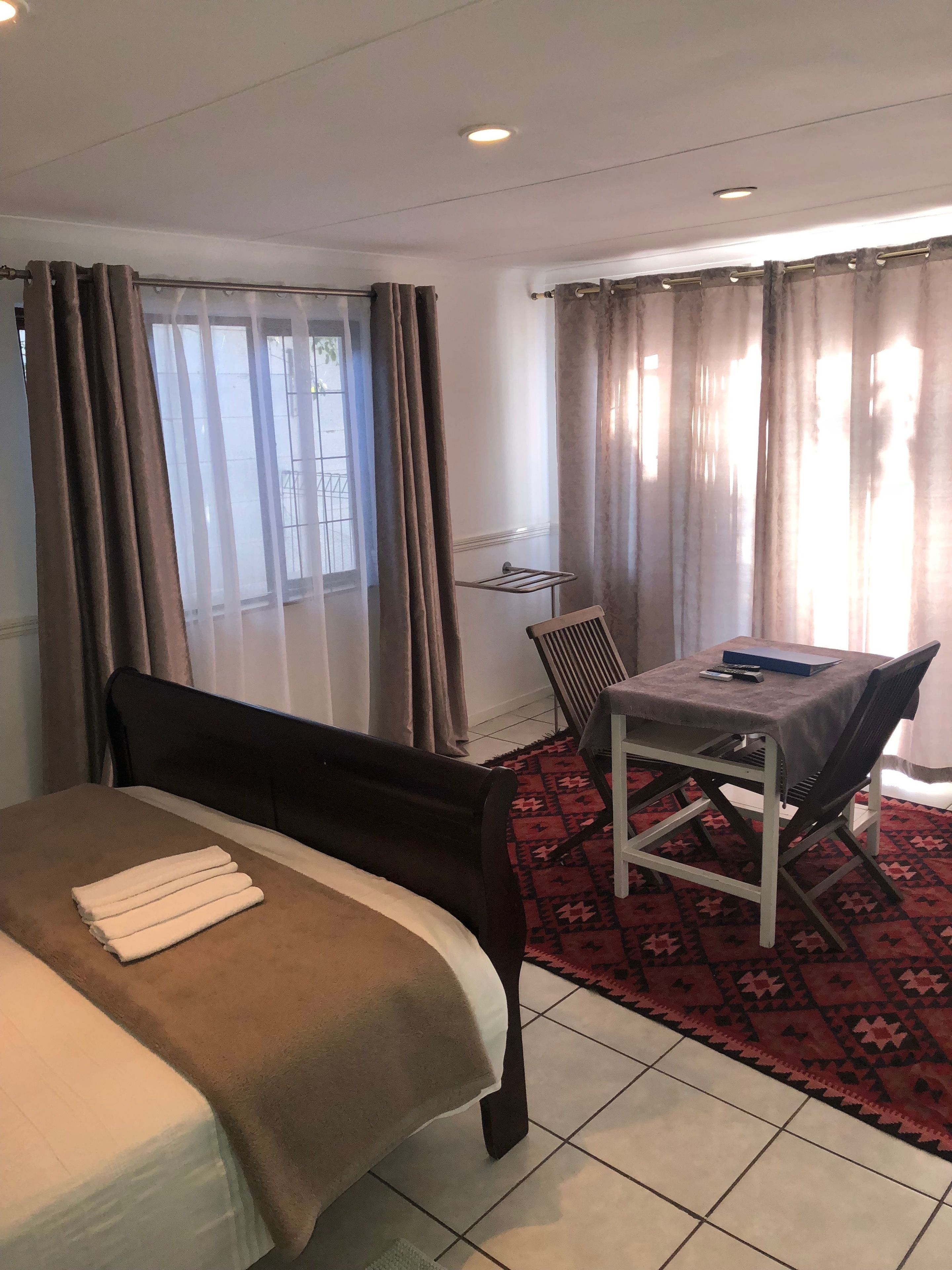 Una habitación de hotel con cama, una mesita pequeña con una silla, un radiador y una ventana con cortinas.