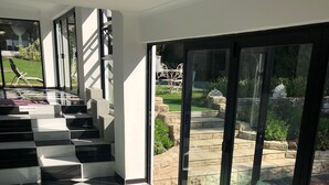 A modern interior with a black and white checkered floor, a staircase, and large glass doors leading to an outdoor garden area. - Muco Guest House (Sandton)