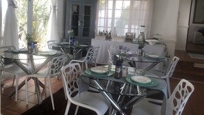 A dining area with round glass tables, white chairs, and a blue cabinet. - Muco Guest House (Sandton)