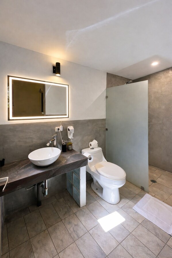 Un baño moderno con un espejo grande, un lavamanos redondo, un inodoro y una ducha con mampara de vidrio.
