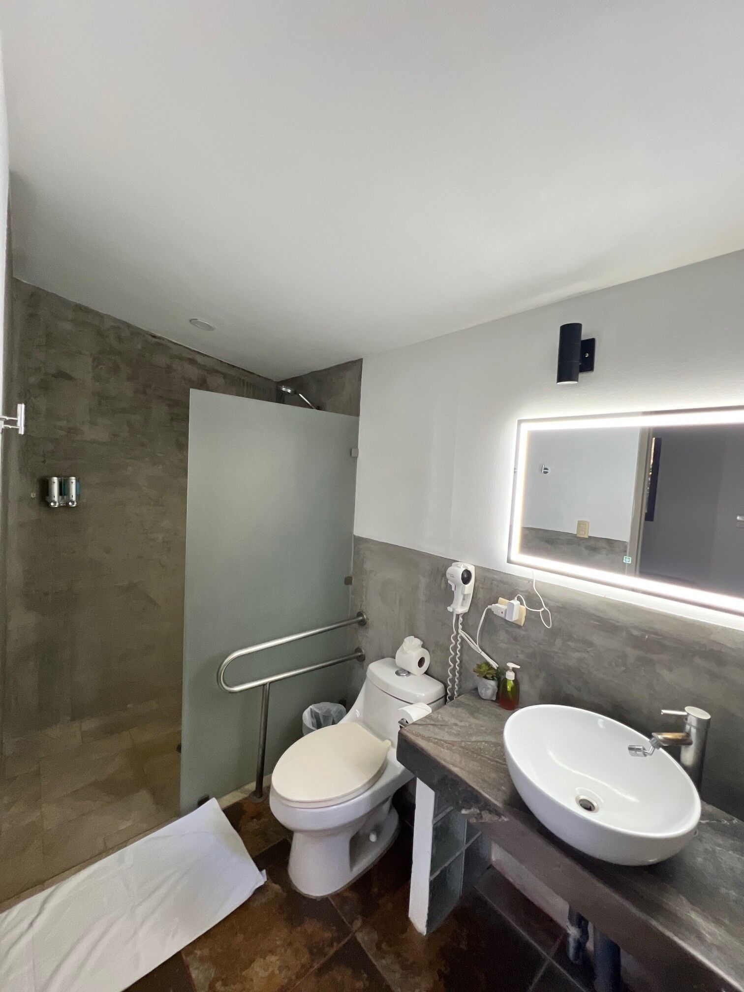 A modern bathroom with a toilet, bidet, and sink, a towel on the floor, and a shower area.
