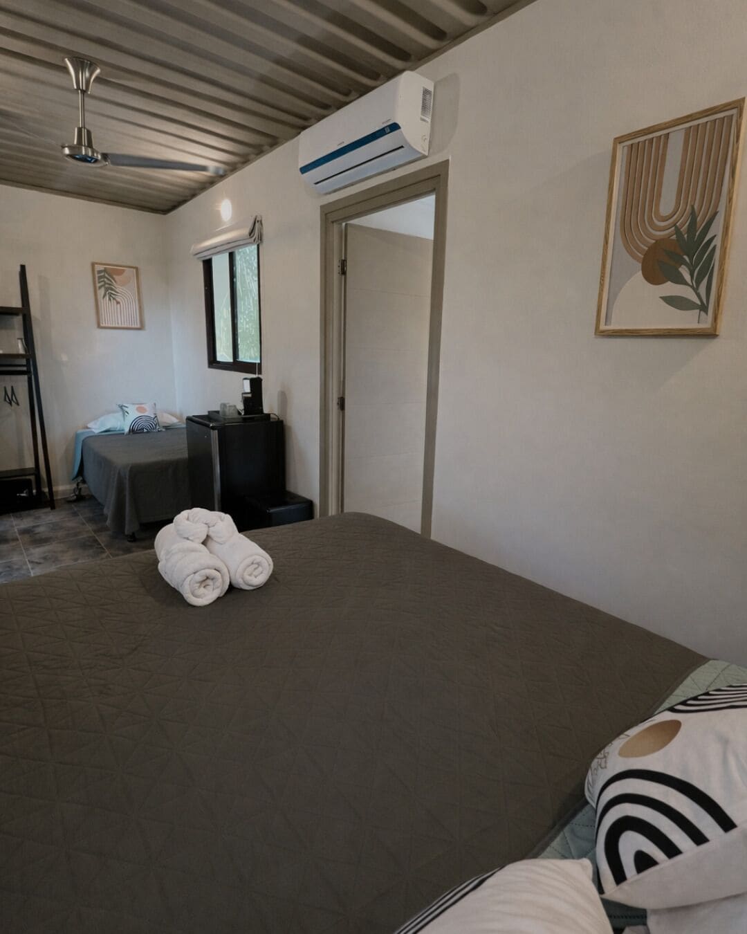 Habitación de hotel con cama, escritorio, aire acondicionado, puerta y un cuadro en la pared.