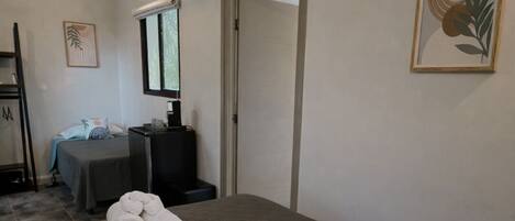 A hotel room with a bed, a desk, an air conditioner, a door, and a framed picture on the wall.