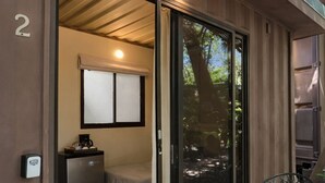A room with a bed, a small kitchenette, a sliding glass door leading to an outdoor area, and a chair outside. - Green Sanctuary Hotel (Nosara)