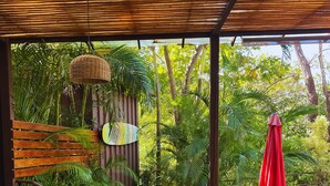 An outdoor patio with wooden tables and chairs, a red umbrella, and lush greenery. - Green Sanctuary Hotel (Nosara)