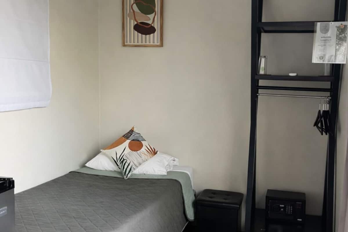 A small, neatly arranged room with a bed, a shelf with keys, a microwave, and a framed picture on the wall.