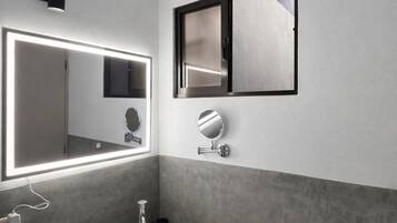A modern bathroom with a large mirror, a round mirror, a built-in sink, and a window above the mirror.