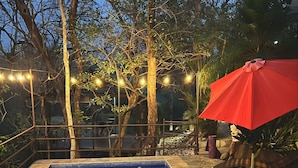 A rectangular swimming pool with a tiled edge, surrounded by trees and a red umbrella. - Green Sanctuary Hotel (Nosara)