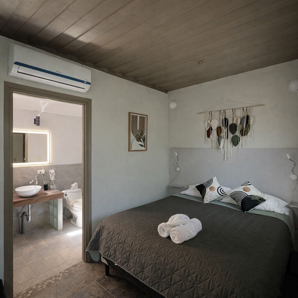 Ein Schlafzimmer mit Bett, Nachttisch, Wandklimaanlage, Badezimmer mit Waschbecken und Toilette sowie einem Spiegel.