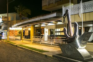 Un restaurante frente al agua con terraza, una gran escultura de metal y un letrero del Hotel Alam.