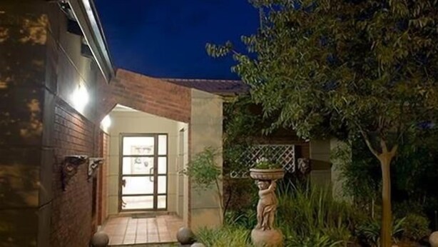 A building entrance with a brick facade, a glass door, and a small garden area with a statue and plants. - Primavera Guest House (Bloemfontein)