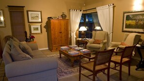 A cozy living room with a sofa, armchairs, a wooden cabinet, and a coffee table with books. - Primavera Guest House (Bloemfontein)