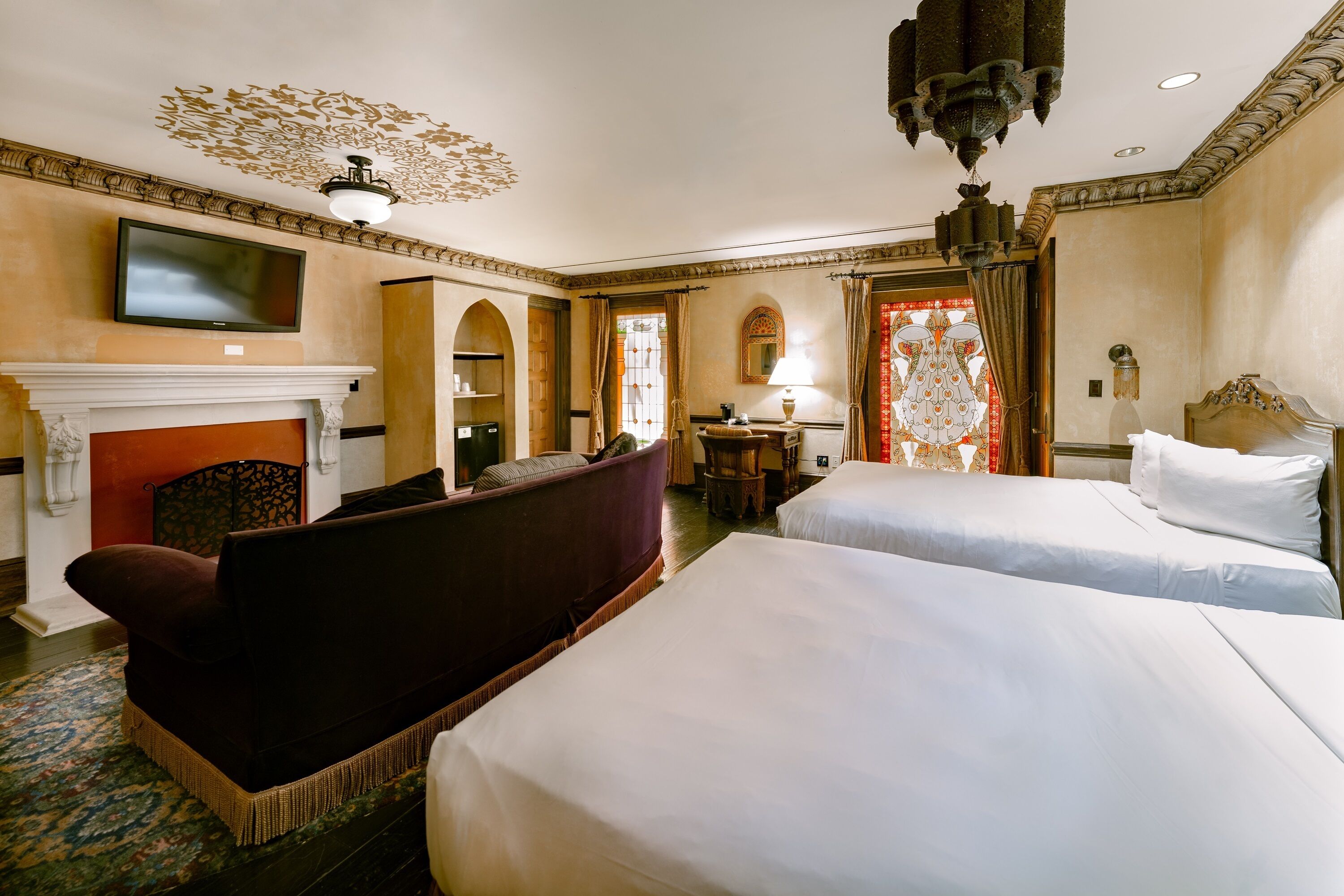 A hotel room with a fireplace, two beds, a sofa, a TV, and a chandelier.